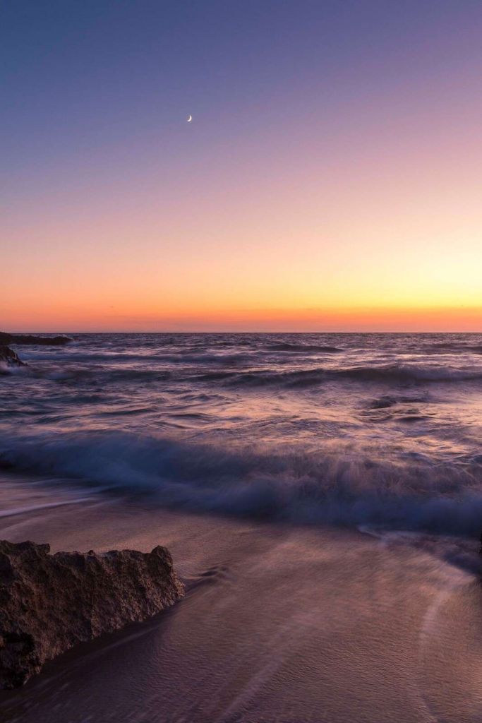 Måneskin over lilla bølger ved solnedgang.