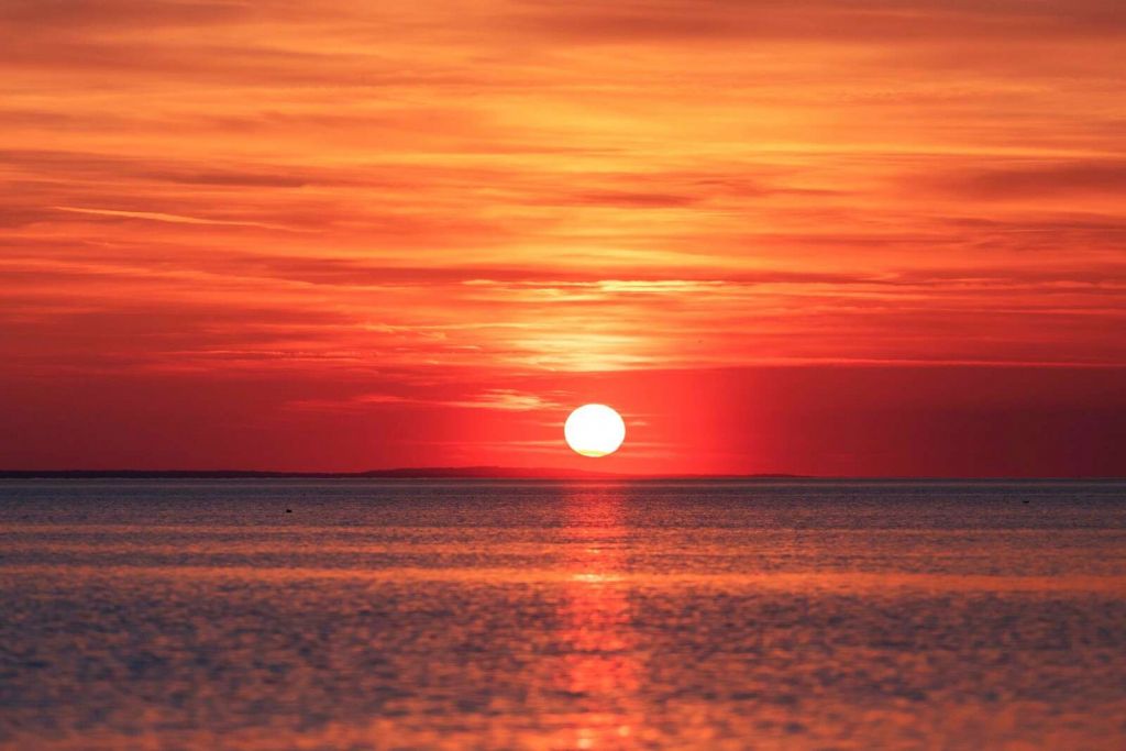 Ildrød solnedgang over stille hav.