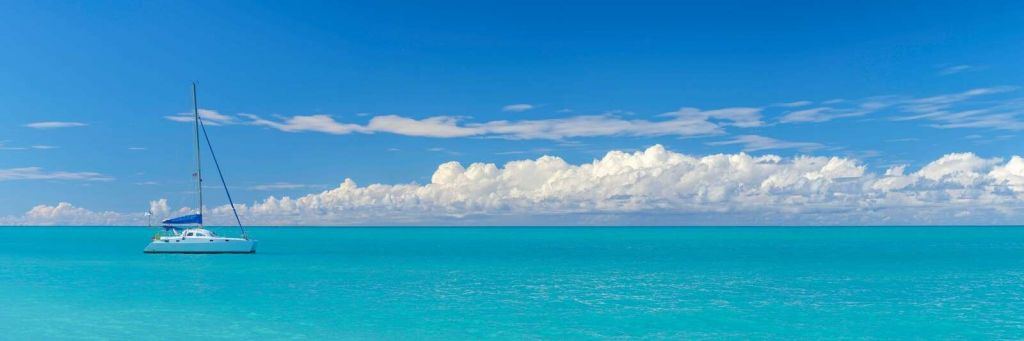 Panoramisk udsigt over et blåt havlandskab med sejlbåd og skyet himmel.