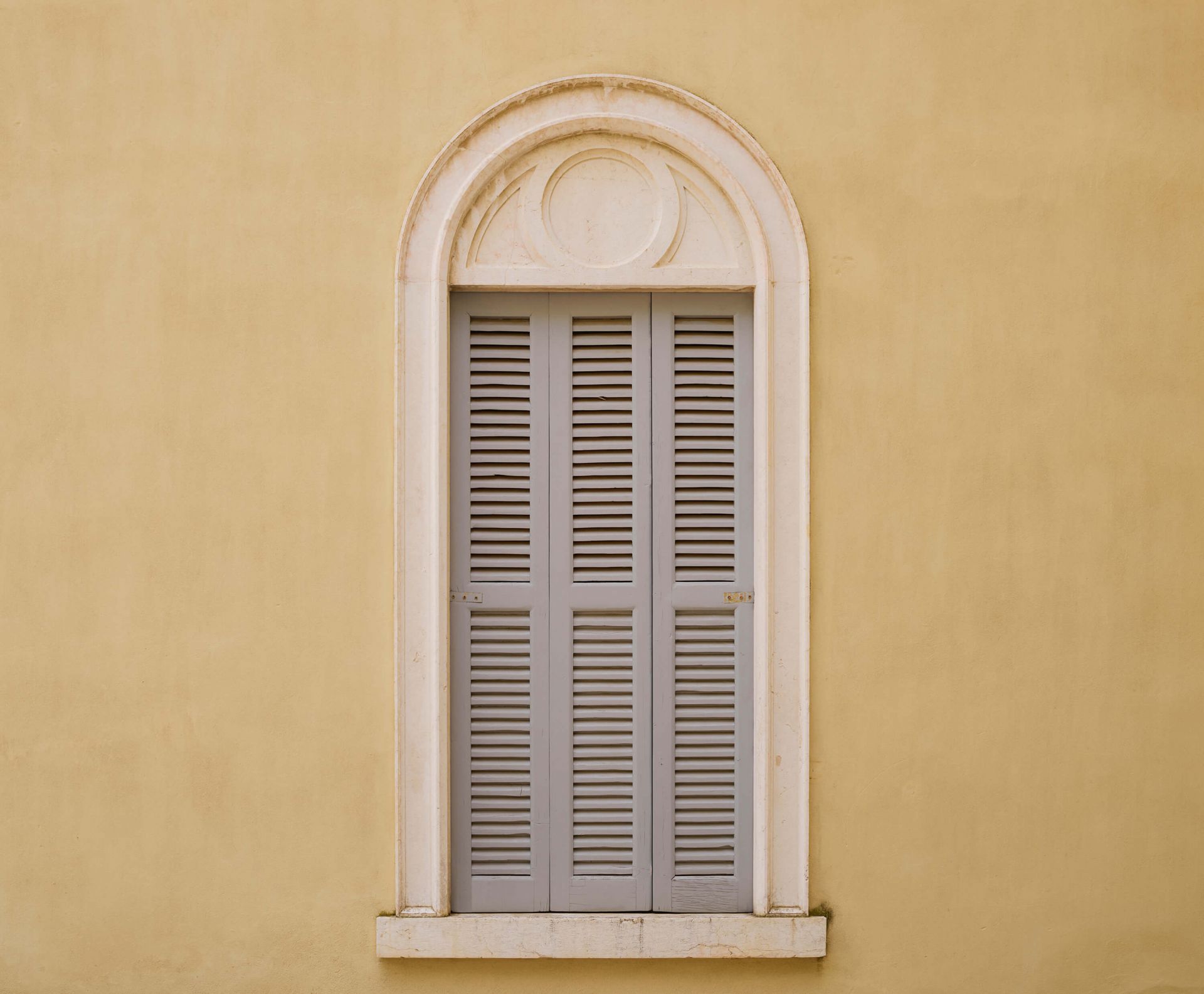 Vindue med træskodder på gul væg